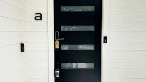 Une porte moderne dotée d’un clavier pour le verrouillage, d’une petite fenêtre et de la lettre « a » peinte sur le mur, à gauche.
