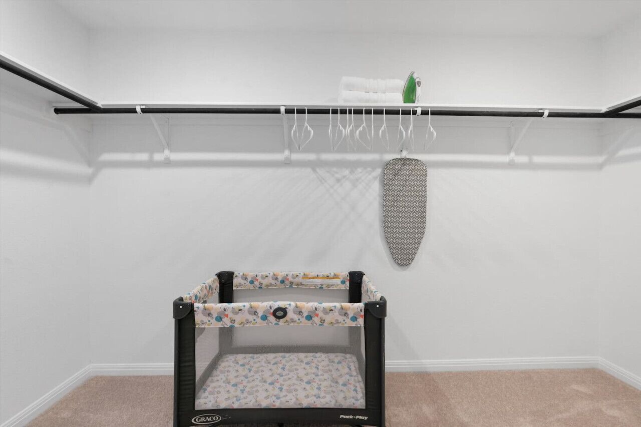 A room with a black playpen, a white shelf with a towel and a green bottle, and a grey patterned object on the wall.