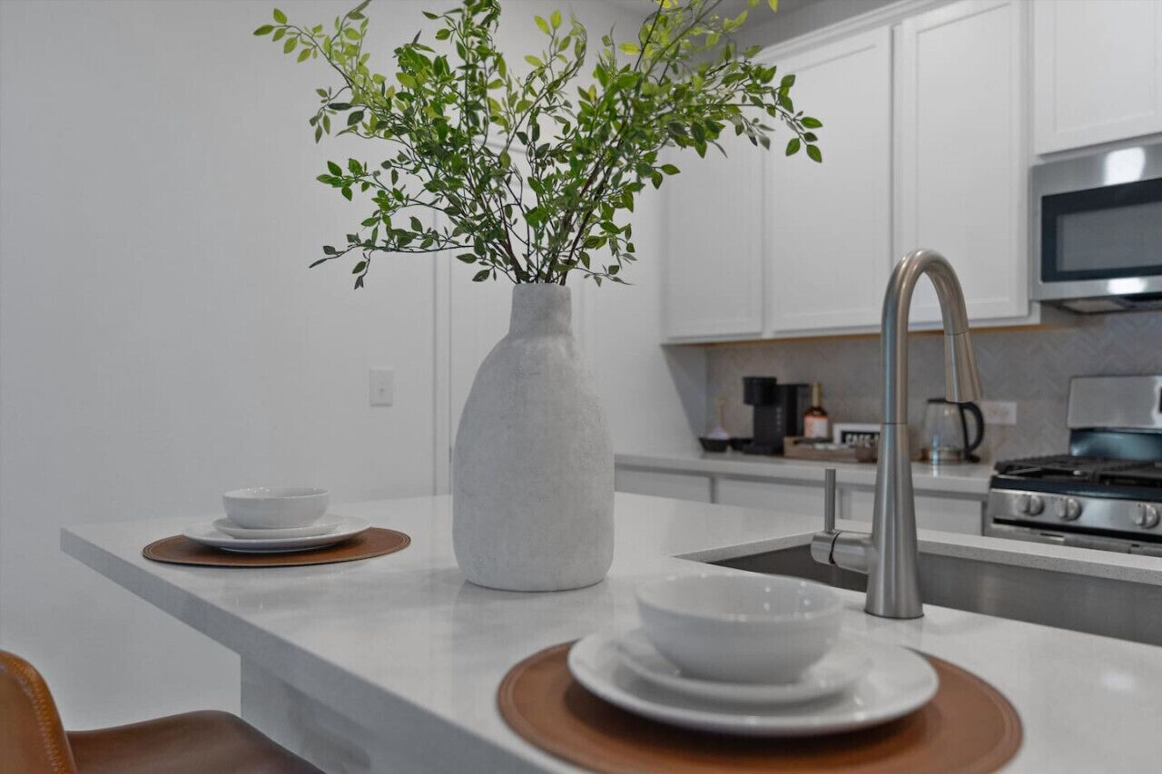 Een moderne keuken met witte kastjes, een roestvrijstalen spoelbak en een vaas met groene planten op het aanrecht.
