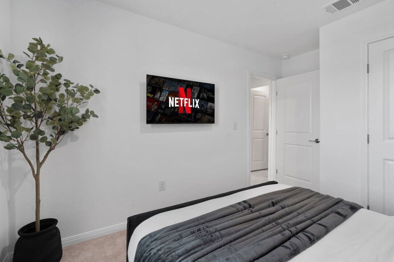 Makuuhuone, jossa on sänky, ruukussa oleva kasvi ja seinälle asennettu televisio, jonka näytöllä näkyy Netflixin logo.