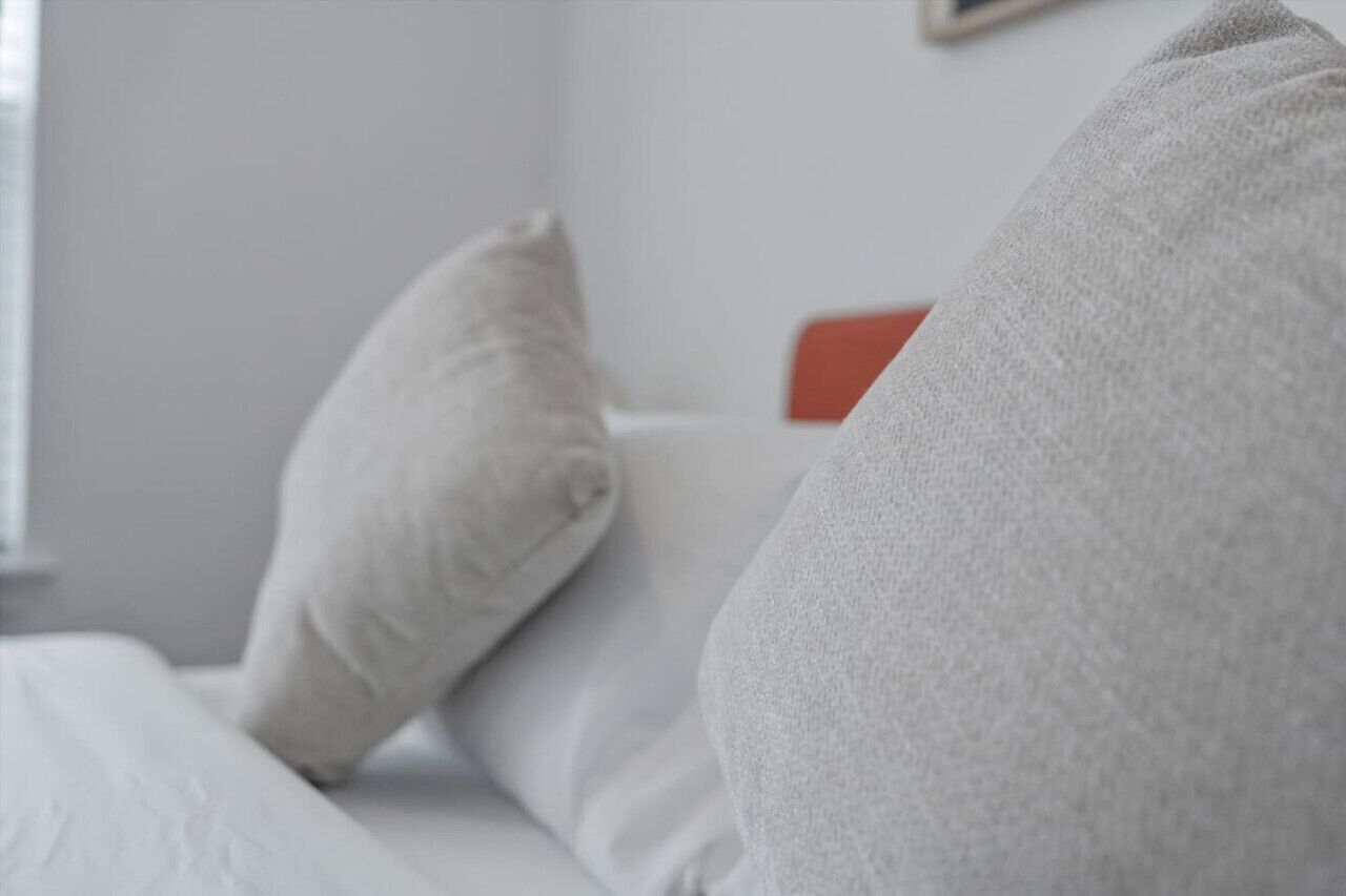 A bed with white bedding and two pillows, one with a red headboard.