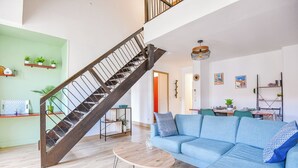 A modern living room with a wooden staircase, a blue sofa, and a dining area.