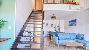 A modern living space with a wooden staircase, a blue sofa, a dining area, and a view of the cityscape.