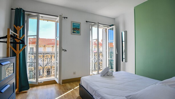 A bedroom with a bed, a green wall, and a view of a balcony with metal railings.
