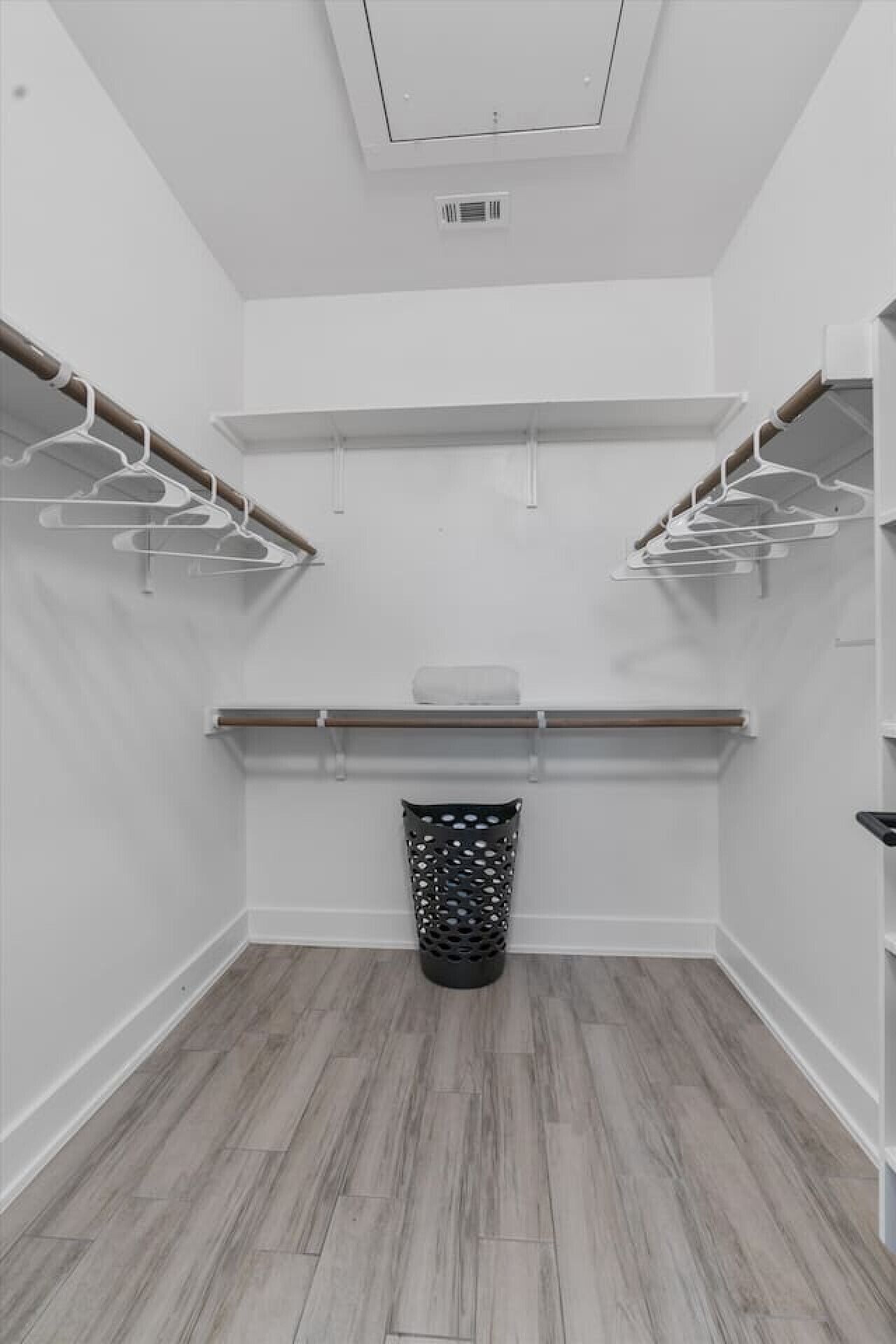 Un dressing accessible sans porte, doté d’un plancher en bois, de murs blancs et d’une bouche d’aération au plafond.