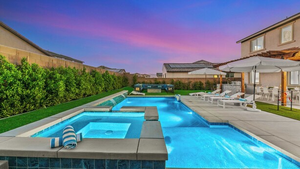 En swimmingpool med jacuzzi, omgivet af en terrasse med liggestole og parasoller.