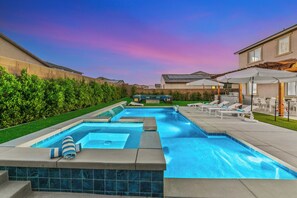 Une piscine avec un jacuzzi, entourée d’un patio aménagé avec des chaises longues et des parasols.