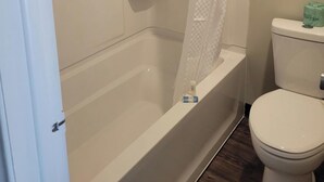 Et badeværelse med badekar, toilet og bruseforhæng.