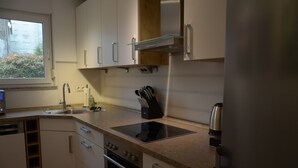 Een moderne keuken met witte kasten, een roestvrijstalen afzuigkap, een ingebouwde oven, een spoelbak en een koffiezetapparaat.