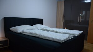Een opgemaakt bed met gestreepte lakens, een donkere hoofdbord en een houten garderobe met twee deuren.