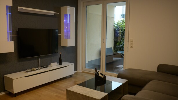 Een moderne woonkamer met een flatscreen televisie, een witte tv-meubel, een glazen salontafel en een bruine bank.