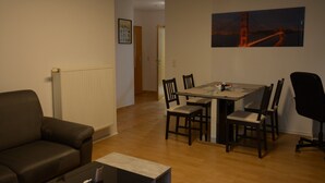 Een woonkamer met een bank, een eettafel met stoelen en een schilderij van een brug.
