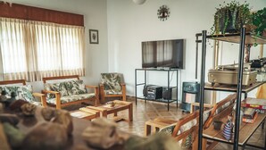 Een woonkamer met een bank, fauteuils, een salontafel, een televisie, een boekenkast en een plant.