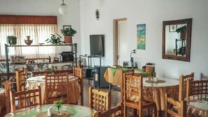 Een eetgedeelte met ronde tafels en houten stoelen, een televisie en potplanten.