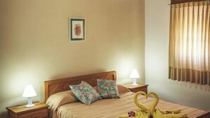 Een knus slaapkamer met een houten plafond, een bed met bloemenkussens, een bedlampje en een handdoekopstelling in de vorm van een hart op het bed.