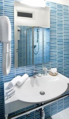 A bathroom with a white sink, blue tiled walls, a mirror, and a towel rack. - Hotel Caravelle (Cattolica)