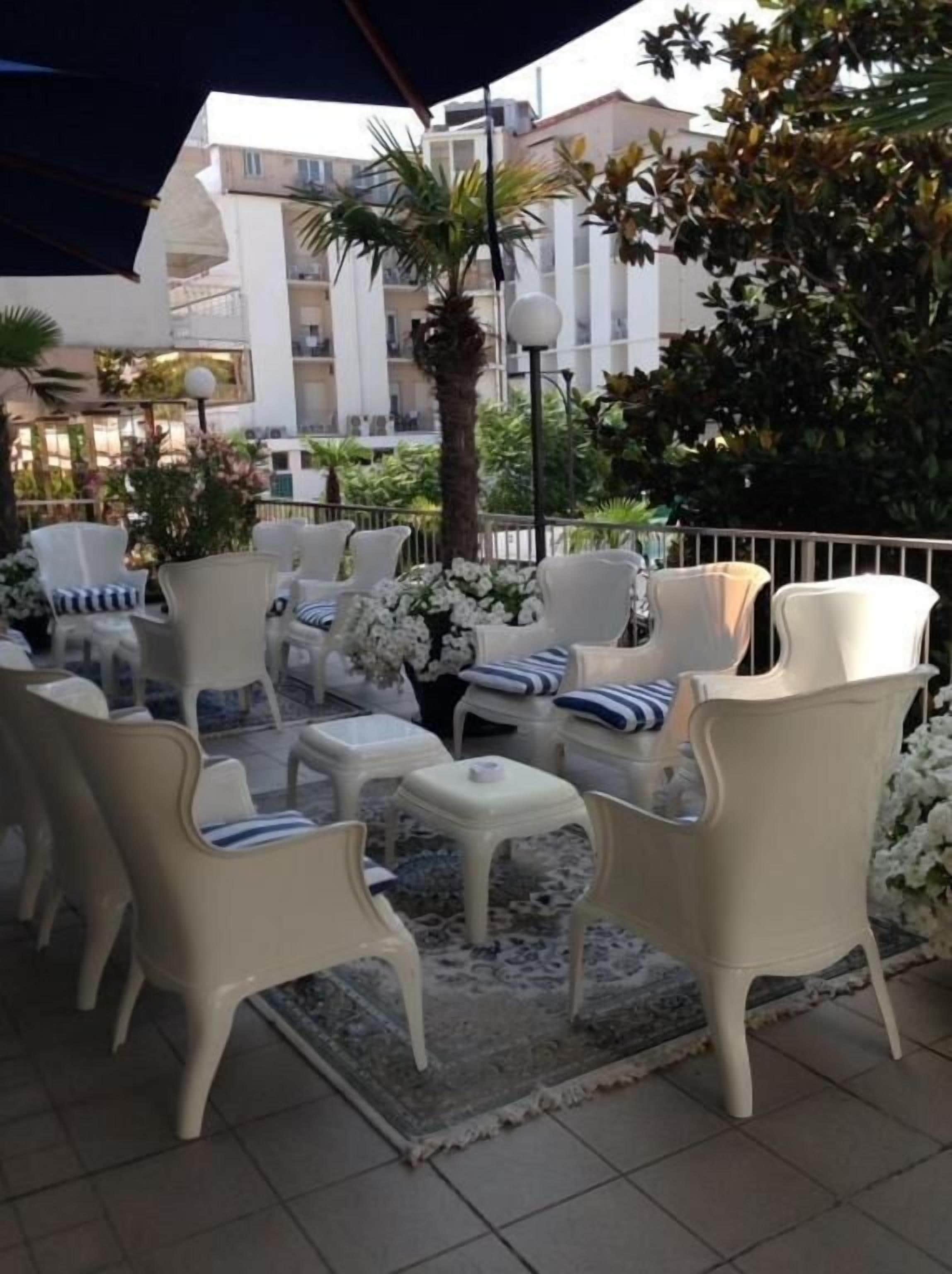 Mobiliario exterior con sillas blancas y cojines azules, una mesa pequeña y una planta decorativa.