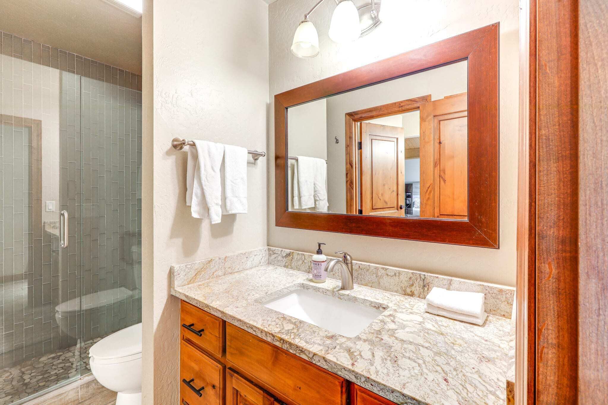 A bathroom with a marble sink, wooden cabinets, a large mirror, and a glass shower enclosure.