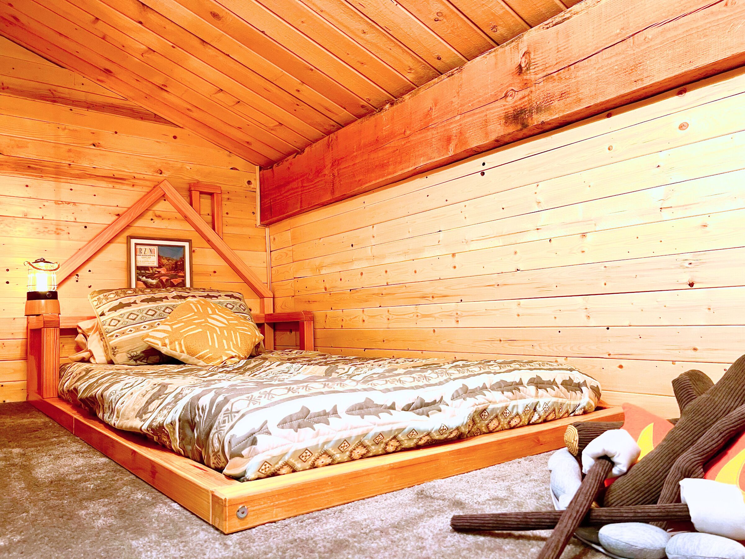 A wooden cabin bedroom with a bed, a framed picture on the wall, and a nightstand with a lamp.