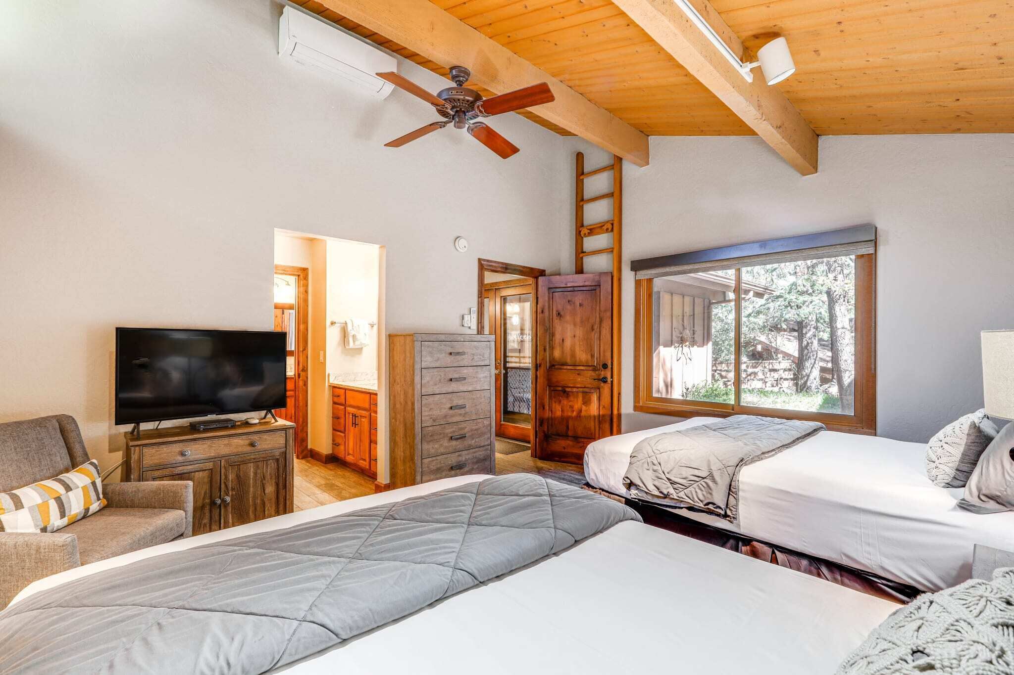 A bedroom with two beds, a TV, wooden furniture, and a large window.