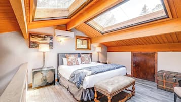 Een slaapkamer met een dakraam, een bed met gestreepte kussens, een bankje en een koffer.