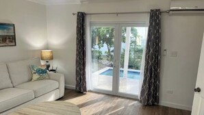 Et værelse med sofa, bord og udsigt til en swimmingpool gennem en glasdør.