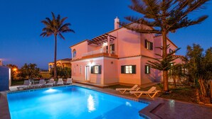 Une maison à deux étages avec une piscine, des chaises longues et des palmiers.
