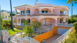 Une maison rose à deux étages, dotée d’un balcon, d’une terrasse couverte et d’un jardin clos.