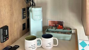 A hotel room with a flat-screen TV mounted above a wooden counter, a Keurig coffee maker, two mugs with motivational quotes, a remote control, and a small photo frame. - Cozy RV with 1 bedroom and WiFi, AC in fantastic Madison (Madison)