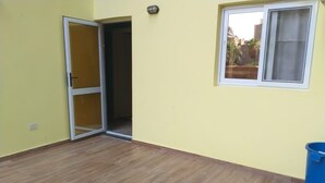 Une pièce avec un plancher en bois, une porte-fenêtre coulissante, une fenêtre avec un rideau et une poubelle bleue.