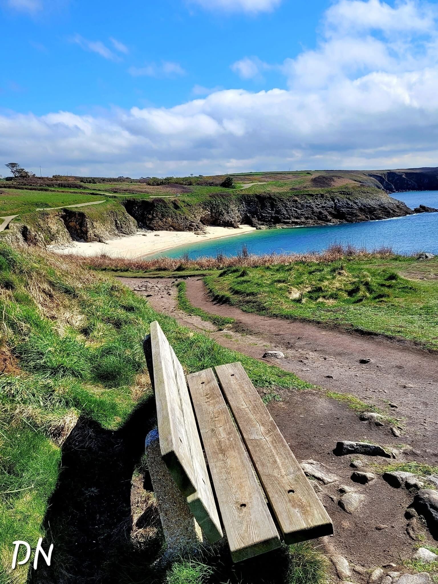 Un banco con vistas a un paisaje costero, una playa de arena y acantilados.