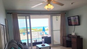 Une chambre avec un lit, un bureau, une chaise, un ventilateur de plafond, une télévision et un balcon avec vue sur l’océan.