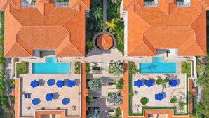 Vue aérienne d’un complexe hôtelier doté de deux piscines, d’espaces de détente et d’un jardin circulaire central.