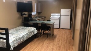 A compact room with a bed, a small kitchenette with a stove and refrigerator, and a television mounted on the wall.
