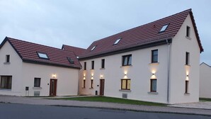 A modern two-story building with a red-tiled roof, multiple windows, and exterior lighting. - Lux Suites Leipzig Luxury Apartment (Leipzig)