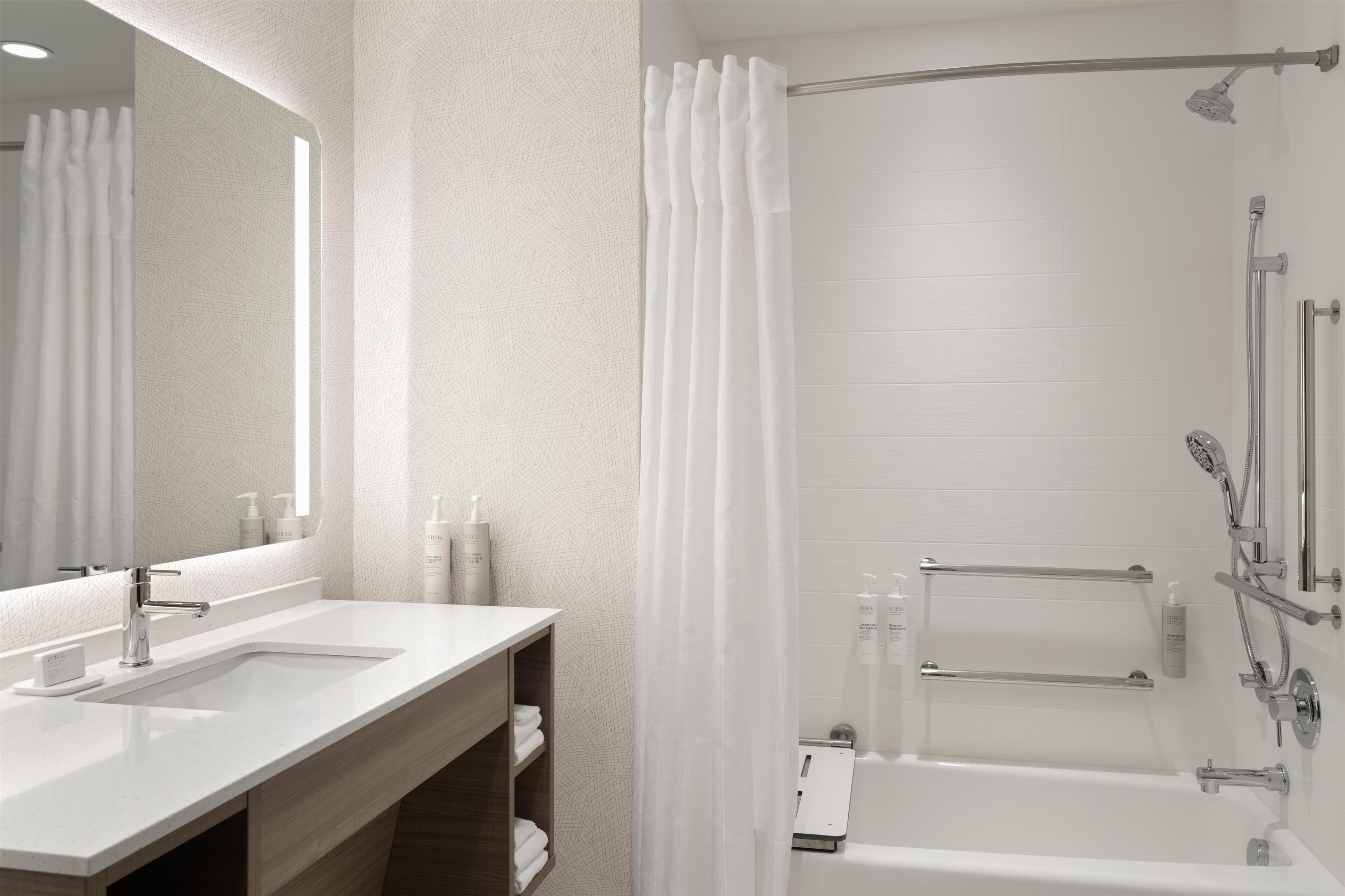 Une salle de bain moderne avec un grand miroir, deux lavabos, une douche avec un pommeau de douche amovible et un porte-serviettes.