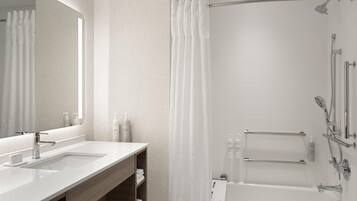 Une salle de bain moderne avec un grand miroir, deux lavabos, une douche avec un pommeau de douche amovible et un porte-serviettes.