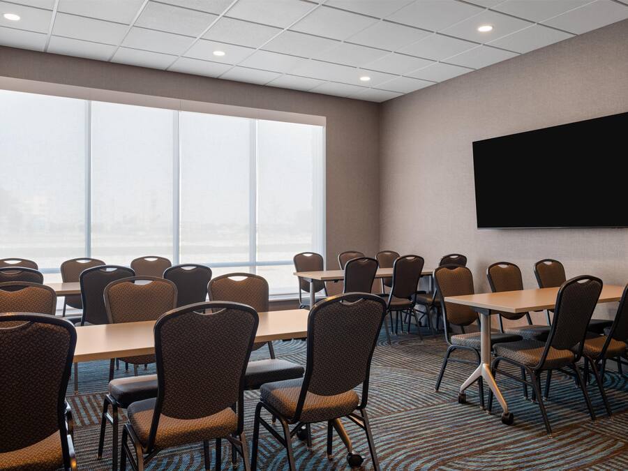 A conference room with large windows, a flat-screen TV, and multiple tables and chairs.