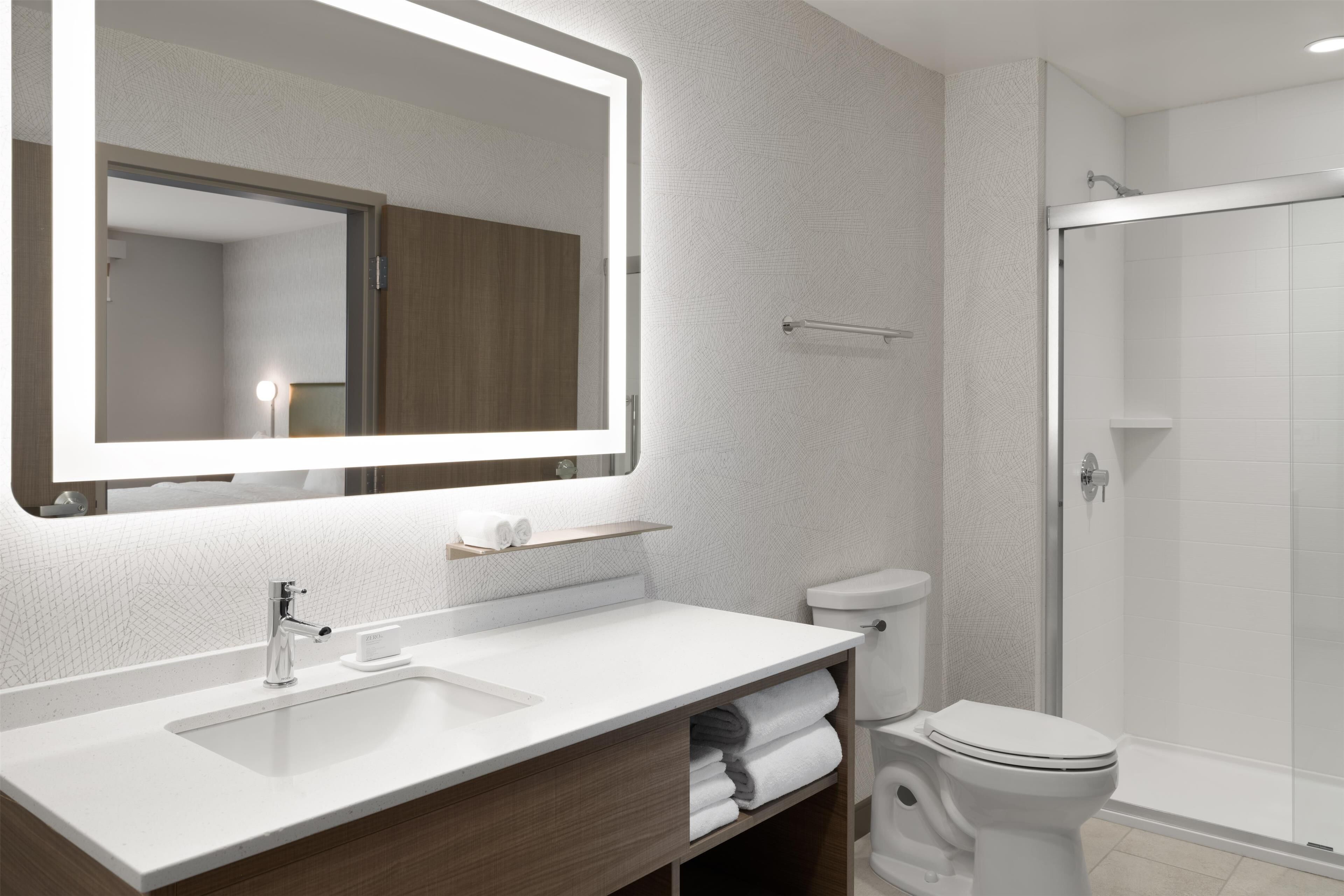 Un baño moderno con un espejo grande, lavamanos blanco y cabina de ducha de vidrio.