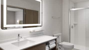 Un baño moderno con un espejo grande, lavamanos blanco y cabina de ducha de vidrio.