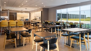 A modern dining area with multiple tables and chairs, large windows offering a view of the outdoors, and a well-lit ceiling with recessed lighting. - Home2 Suites By Hilton Kearney (Kearney)