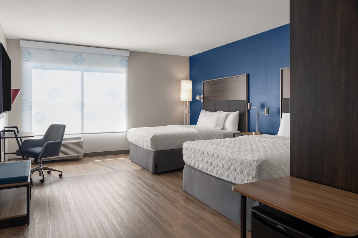 Une chambre d’hôtel avec deux lits, un bureau, une chaise et une grande fenêtre donnant sur un beau paysage.