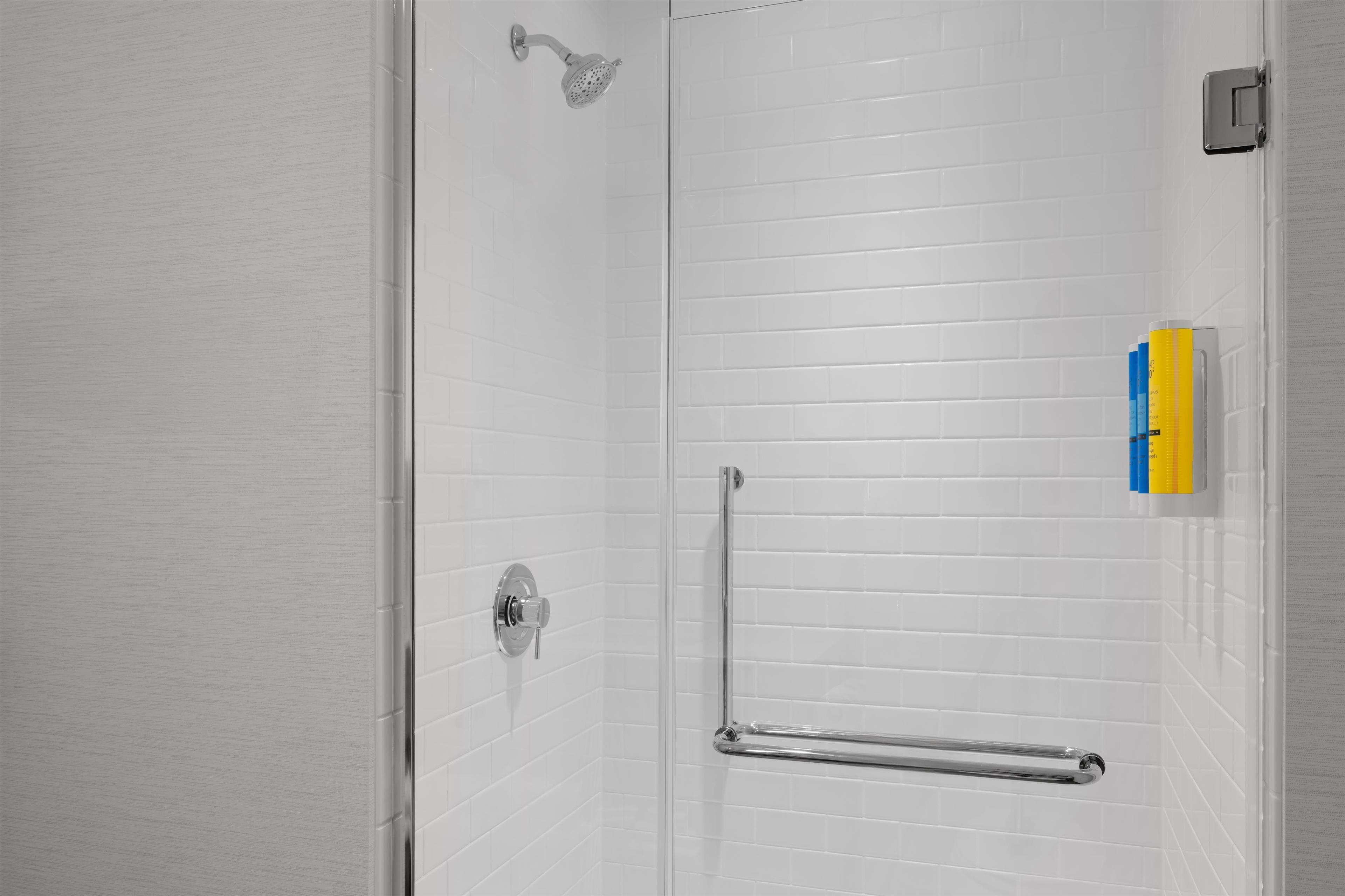 A shower with a handheld showerhead, a grab bar, and a soap dispenser on the wall.