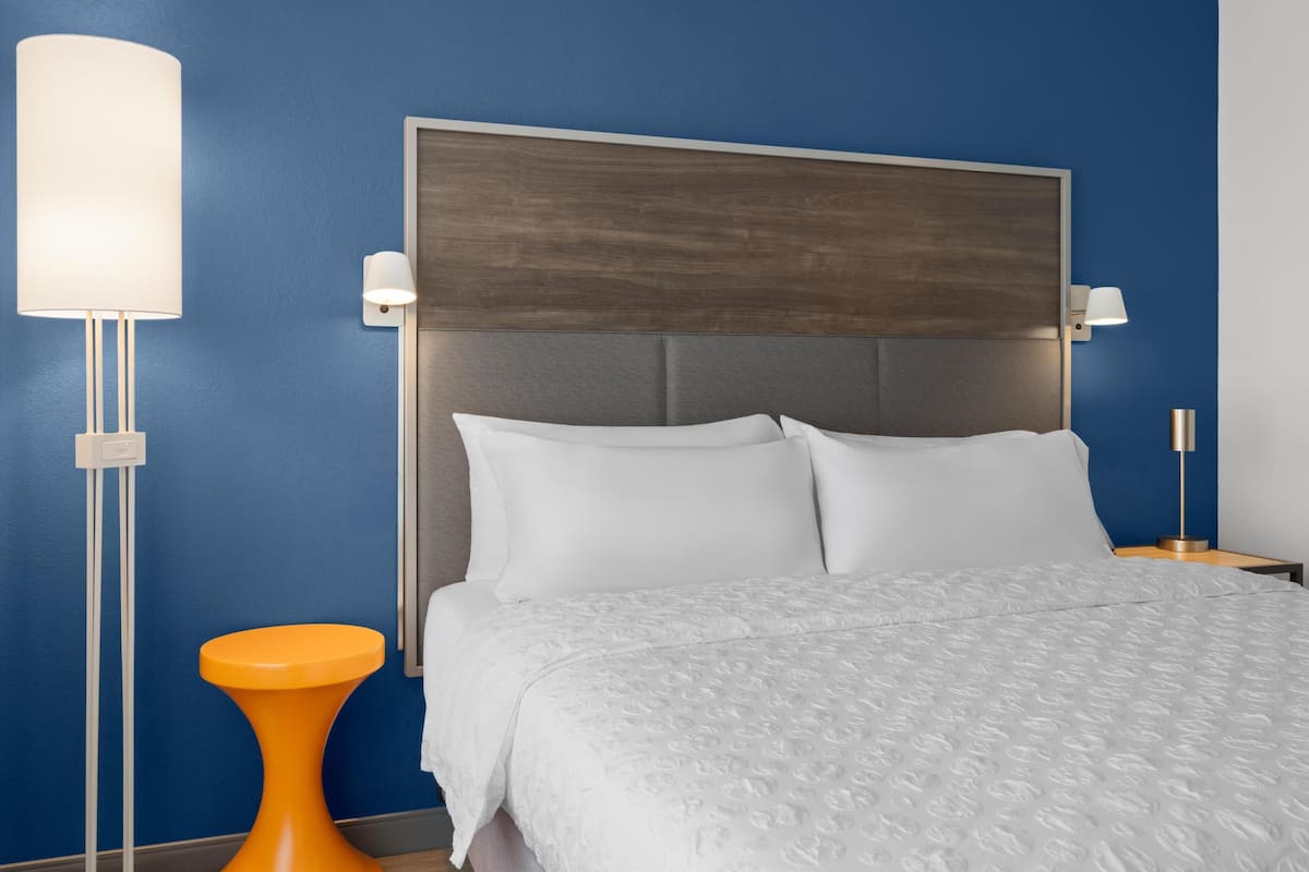 Une chambre d’hôtel avec un grand lit, une table de chevet, une lampe et un petit tabouret orange.