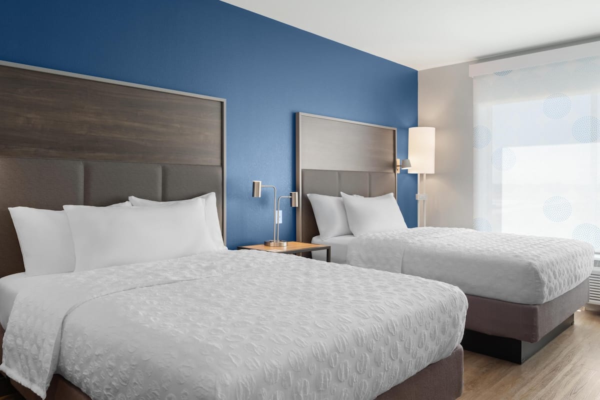 Une chambre d’hôtel avec deux lits, une table de chevet, une lampe et une fenêtre donnant sur un beau paysage.