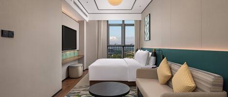 A hotel room with a bed, a sofa, a television, a window with a view, and a patterned rug.