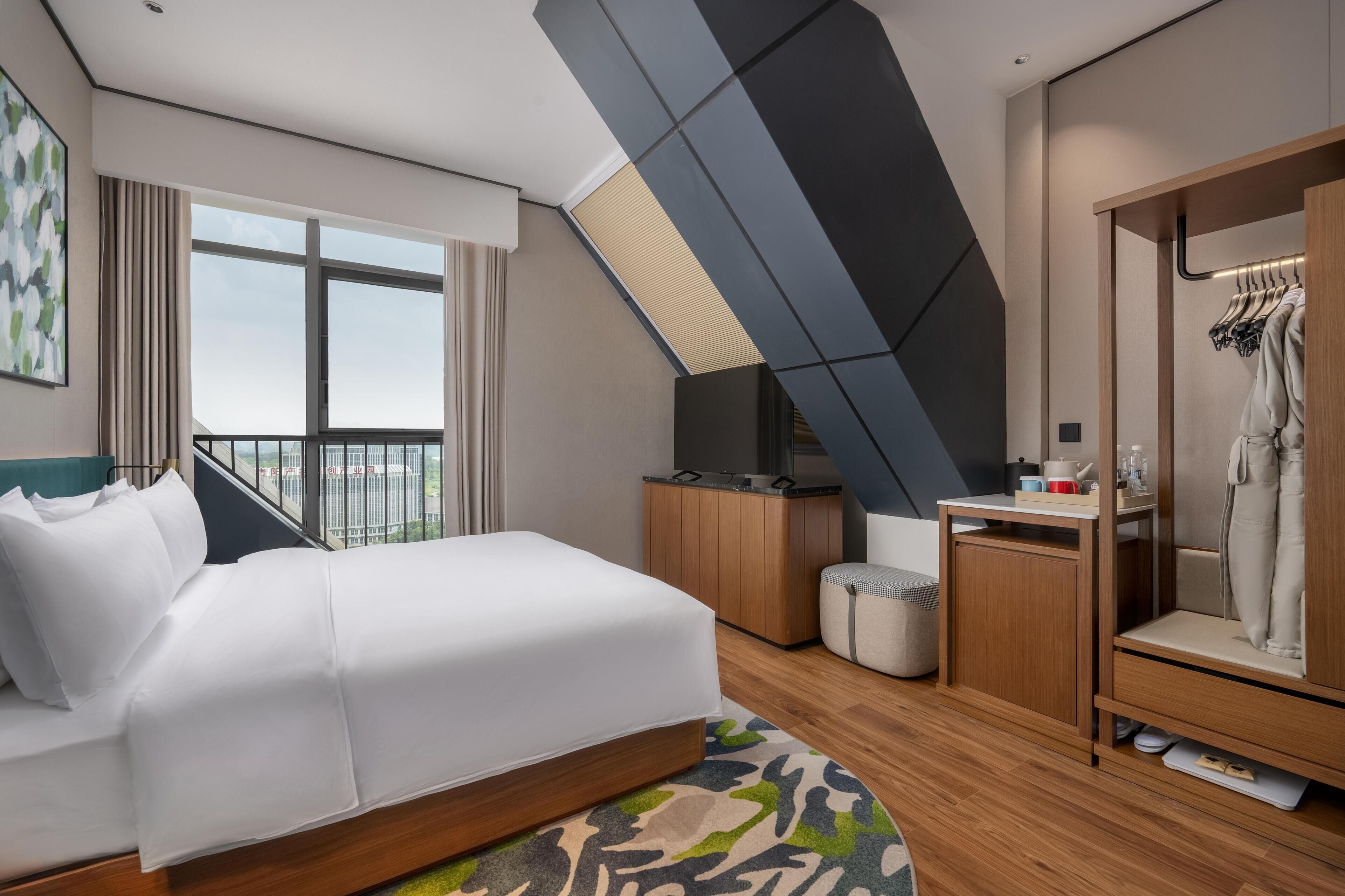 Una habitación de hotel moderna con una cama grande, un escritorio, un armario y vistas a la ciudad.