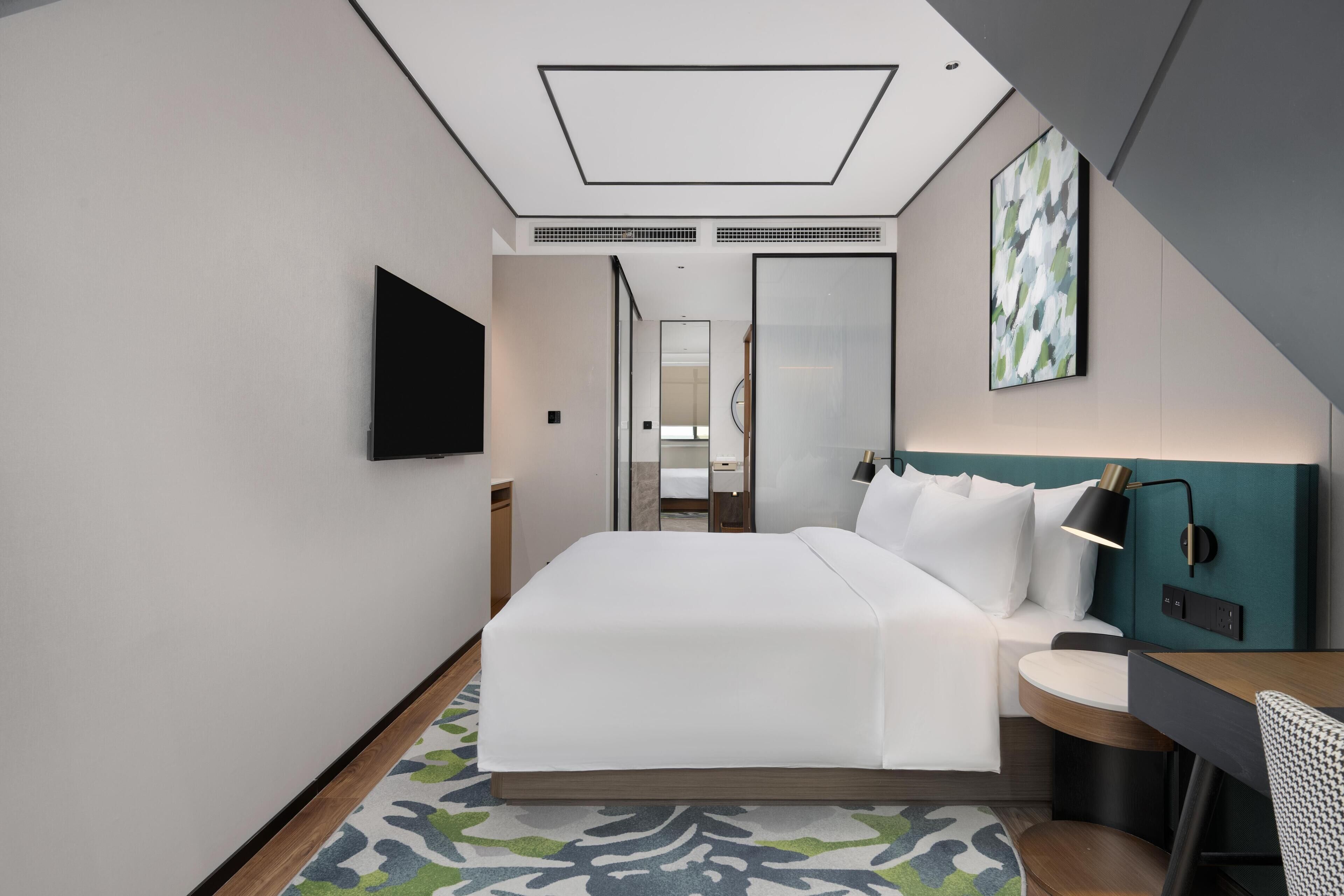 Een moderne hotelkamer met een groot bed, een bureau, een stoel, een televisie en een schilderij aan de muur.