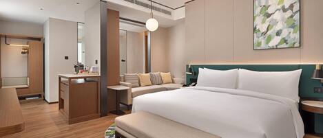 A modern hotel room with a large bed, a desk, a seating area, and a bathroom.