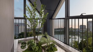 Een balkon met uitzicht op een meer en gebouwen, met een bloemenpottenopstelling en een metalen hekwerk.